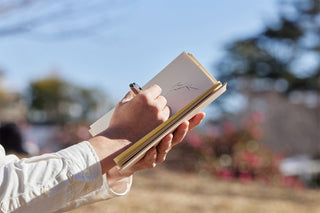 Beige hard-cover A5 notebook held open by hand, pages visible