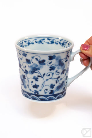 Blue and white floral-patterned mug held by a hand on a white background