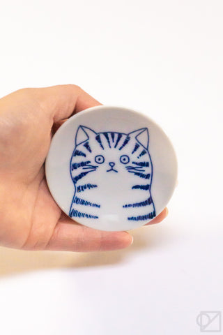 Hand holding a small white ceramic dish with a cat illustration on a white background
