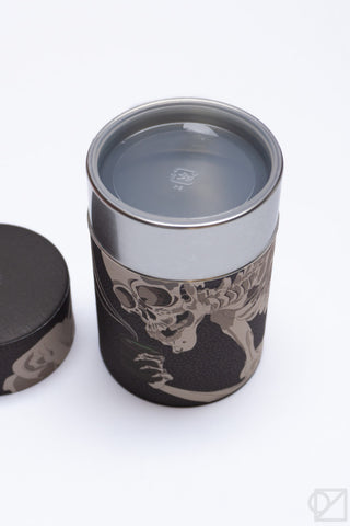 Dark tea canister with skeleton graphic, top view with open metal interior