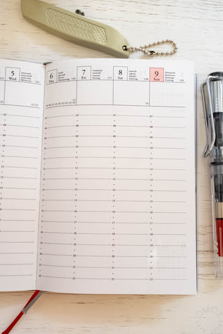 Opened planner showing vertical hourly layout and stationery items on table