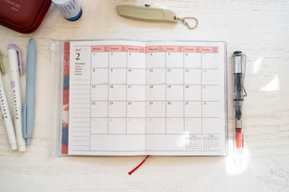 Opened planner showing monthly layout with stationery items on table