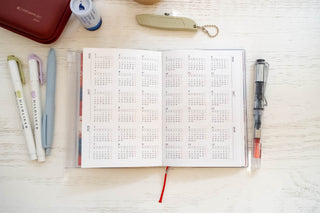 Opened planner showing yearly calendars with stationery items around table