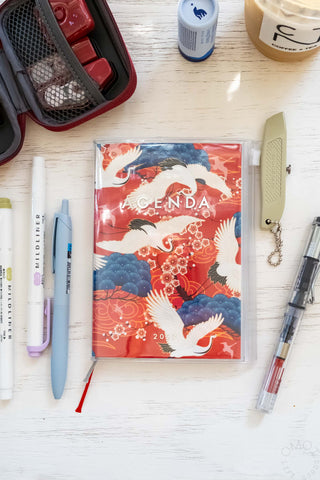 Red planner with birds and flowers on a table with stationery items around