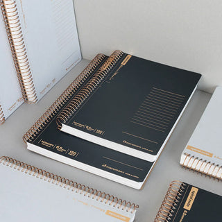 Black spiral-bound notebook with gold accents on a light gray surface
