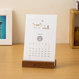 2027 cat illustrated desk calendar on wooden stand, showing monthly grid and month label