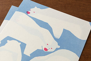 Two envelopes with white polar bear illustrations on a blue background, placed on a wooden surface.