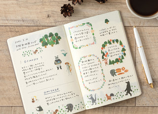 Open notebook with decorative pages on a wooden surface with a pen and coffee cup.