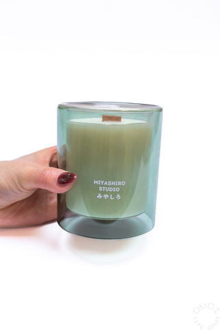 Hand holding a green candle with 'MIYASHIRO STUDIO' branding on a white background