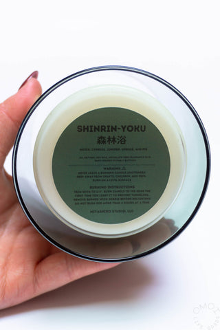 Hand holding a Shinrin-Yoku candle with instructions and warning label on a white background