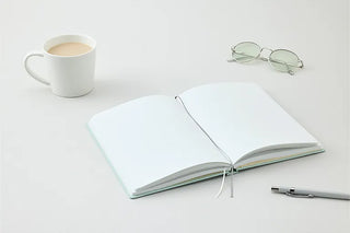 Open dot grid notebook with pale mint cover, pen, glasses, and cup
