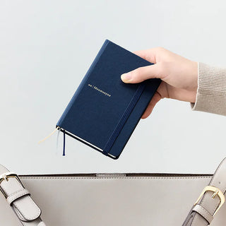 Navy hard cover dot grid notebook held in hand with elastic closure