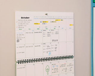 Wall planner calendar with October month displayed and writing on a beige wall.