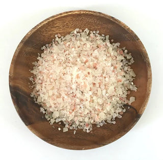 Wooden bowl filled with pink and white bath salts on a white background