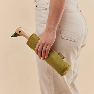 Person holding a green duck-shaped umbrella with a beige background