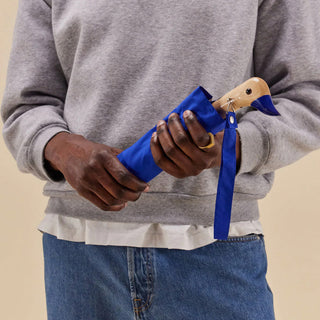 Person holding a blue duck umbrella against a neutral background