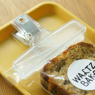 Close up of a clear penco binder clip holding a package of bread.