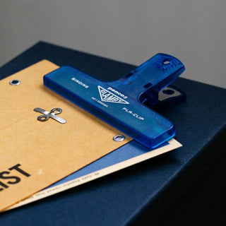 Clear blue penco binder clip holding together paper on a dark blue surface