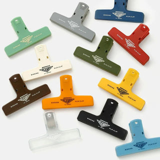 Penco binder clips of various colors spread on a white background