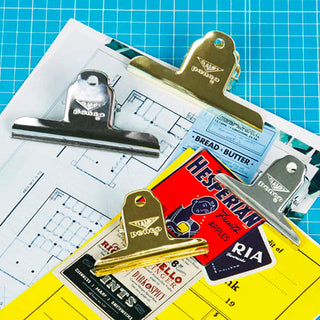 Gold binder clip holding papers and cards on a blue grid work surface