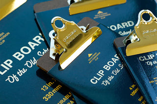 Close-up of several navy blue clipboards with shiny gold metal clips. The clipboards show text  'CLIP BOARD Of the Old School'.
