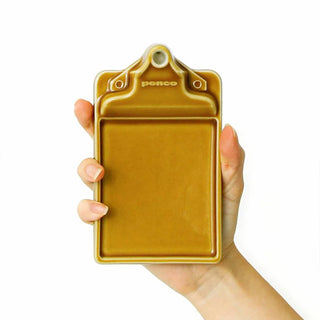 Hand holding a brown/yellow ceramic clip board with 'Penco' branding on a white background