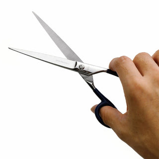 Large stainless steel scissors held in hand, green finger loops and silver blades