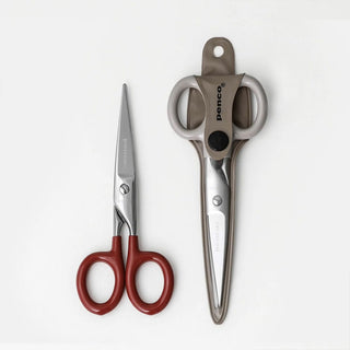 Small stainless steel scissors with red handles and gray protective sheath