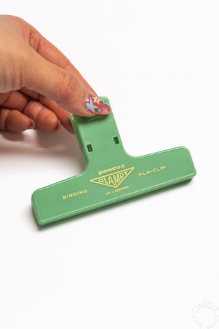 A hand holding a mint penco binder clip on a white background