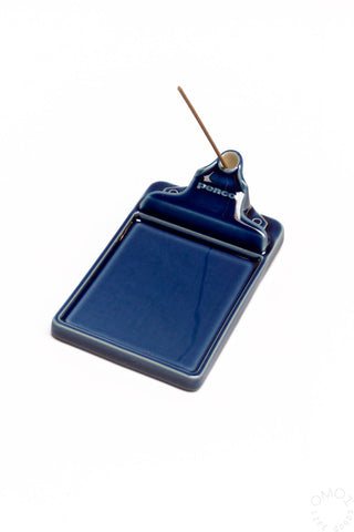 A dark blue ceramic incense holder with a single incense stick inserted, on a white background.