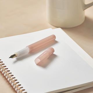 Translucent pink Kakuno Madoromi fountain pen with gold nib on notebook