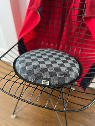 Round checkerboard seat pad with black edge, shown on a metal rack