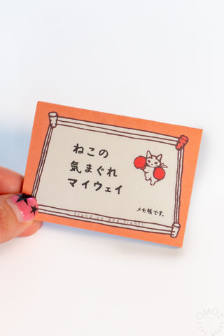 Small orange memo pad with Japanese text and a cat illustration held by a hand.