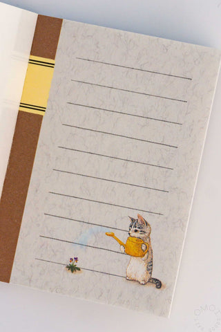 Notebook with a cat watering plant illustration on a white surface