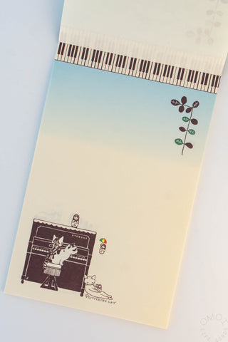 Memo pad pages with cats around a piano watching a Matryoshka doll fall with a tiny umbrella