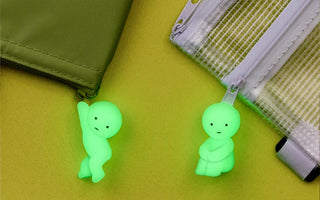 Two pale green glow-in-the-dark zipper charms on green bag