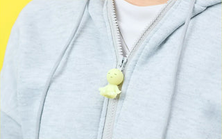 Pale yellow zipperbite figurine charm hanging from a light gray hoodie zipper