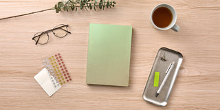 Notebook, pen, coffee cup, and glasses on a wooden surface