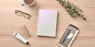 Desk with white notebook, phone, glasses, and tea cup on a wooden surface