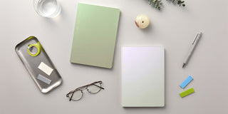 Desk setup with notebooks, glasses, and stationery on a light surface