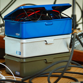 Stack of blue, silver, and green metal toolboxes with cables on a wooden surface.