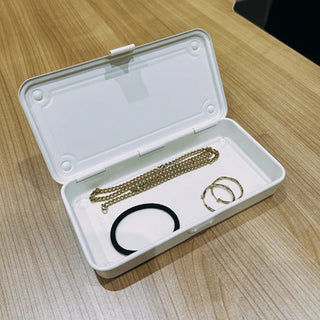 White trunk toolbox open with jewelry items inside on a wood table.
