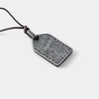 Rectangular pewter charm tag with stitched border and dark leather cord