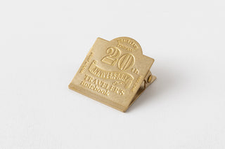 Gold metal clip with '20th Anniversary Traveler's notebook' text on a white background