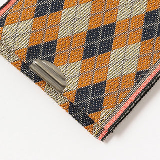 Close-up of a woven fabric with geometric pattern and a metal clip on a white background
