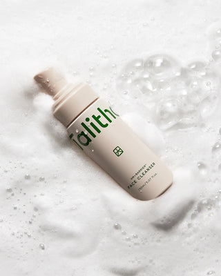 Beige face cleanser bottle lying on white foam with bubbles