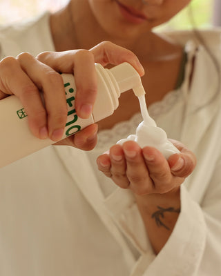 Hands dispensing white cleanser foam from a pump bottle onto palms