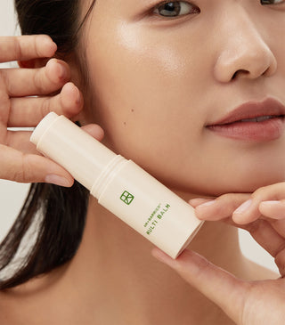 Balm stick applied along face near lips; beige tube with green logo