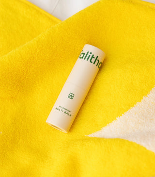 Beige Multi Balm stick resting on yellow towel, showing green logo label