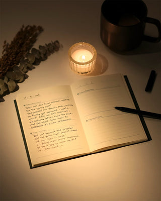 Open notebook with writing, lit candle, and pen on a table